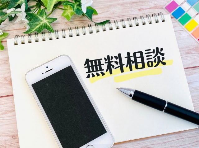 「無料相談」と書かれたメモとスマートフォンを並べた、問い合わせや相談を促すイメージ