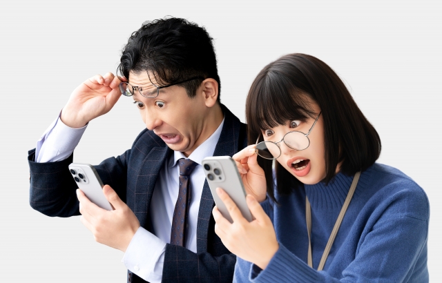 スマートフォンの画面を見て、想定外の内容に驚いている男女の様子