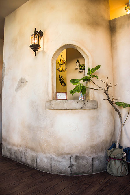 塗り壁仕上げの壁面にアーチ型ニッチと照明を設けた、世界観のある店舗内装デザイン