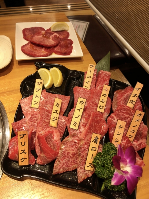 部位名の札が添えられた上質な焼肉の盛り合わせ。レモンと花のあしらいで彩られた美しい肉皿のクローズアップ