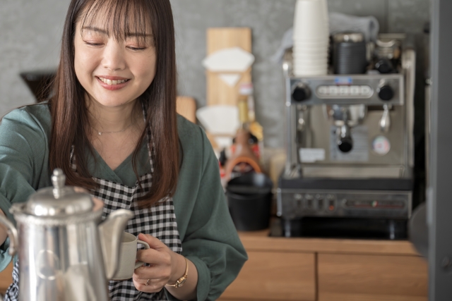 エスプレッソマシンのあるカウンターで、ポットを手に微笑むカフェスタッフの様子