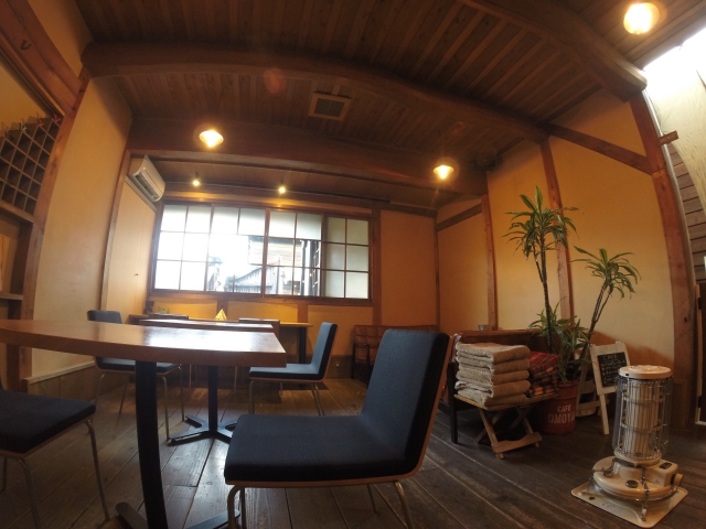 木の梁と無垢材の床が印象的な和風の店内。落ち着いた照明と観葉植物、石油ストーブが置かれた温かみのある空間