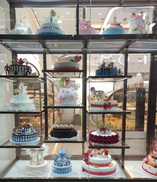 ショーケースに並べられたデコレーションケーキの数々。キャラクターや誕生日モチーフなど華やかなデザインのケーキがガラス越しに展示されている